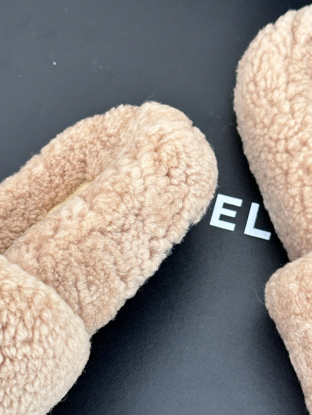 Beige plush shearling slide slipper close-up on black box, womens luxury shoes