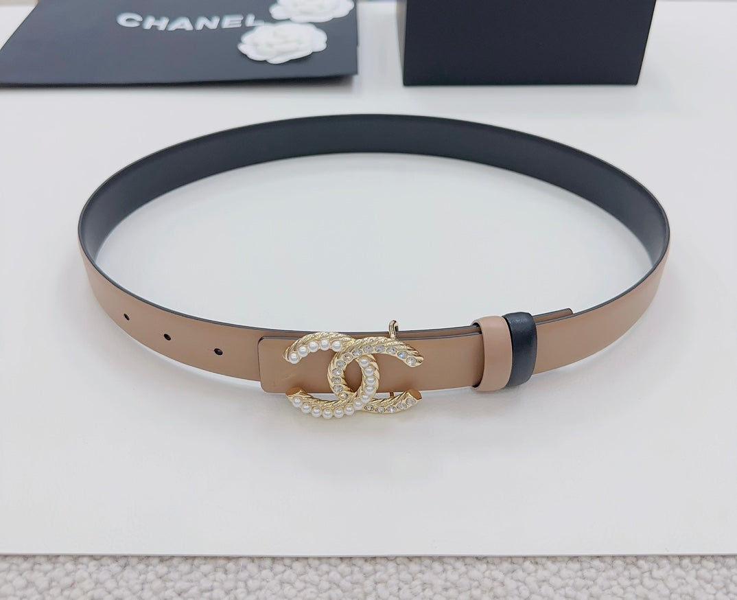 Tan leather belt with navy underside and gold-tone double-C crystal buckle, laid flat