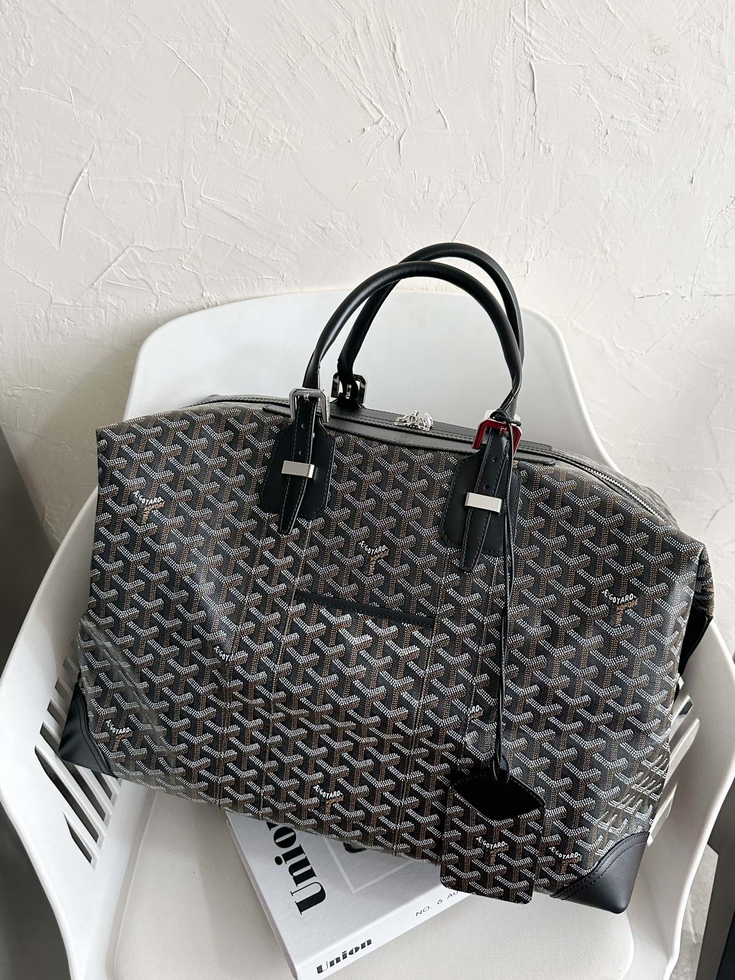 Tote bag with dark monogram pattern, black top handles, and zipper top closure.