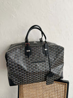 Tote bag with dark monogram pattern, black handles, and side leather strap detail.