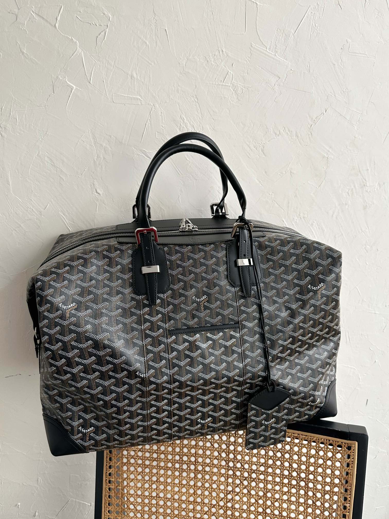 Tote bag with dark monogram pattern, black handles, and side leather strap detail.