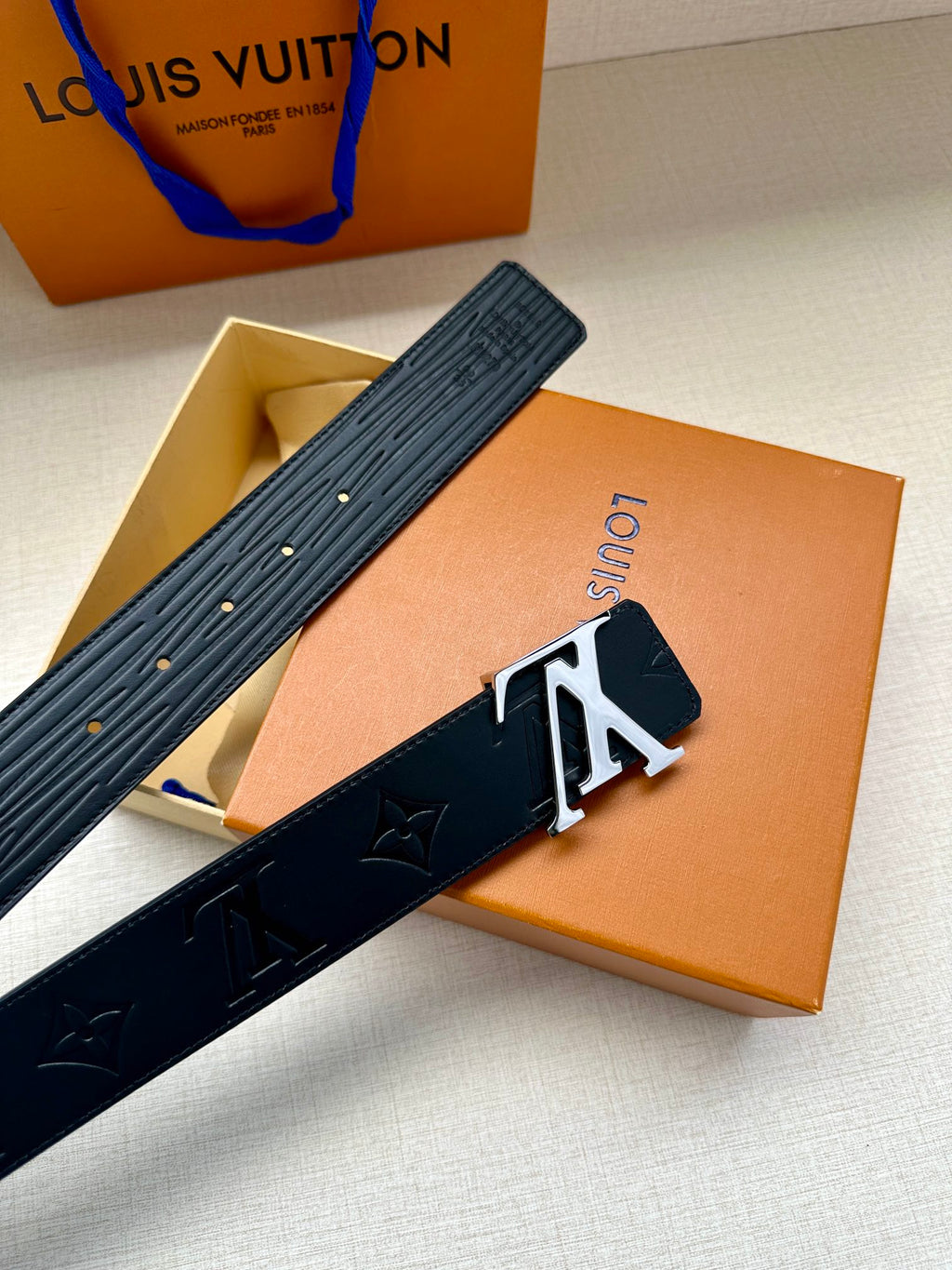 Louis Vuitton belt folded view in dark blue, textured strap with gold-tone LV buckle.