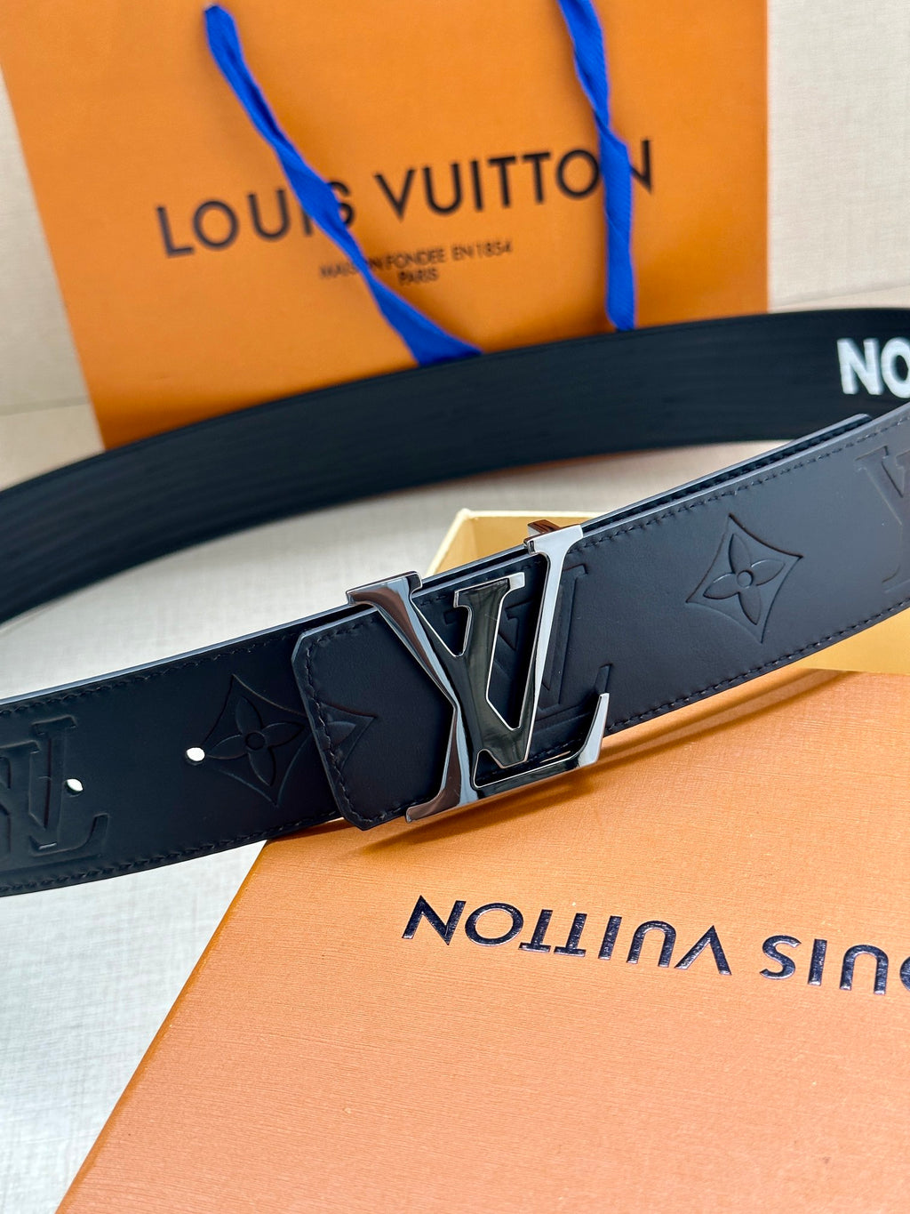 Louis Vuitton belt close-up: dark blue embossed monogram with gold-tone buckle centerpiece.