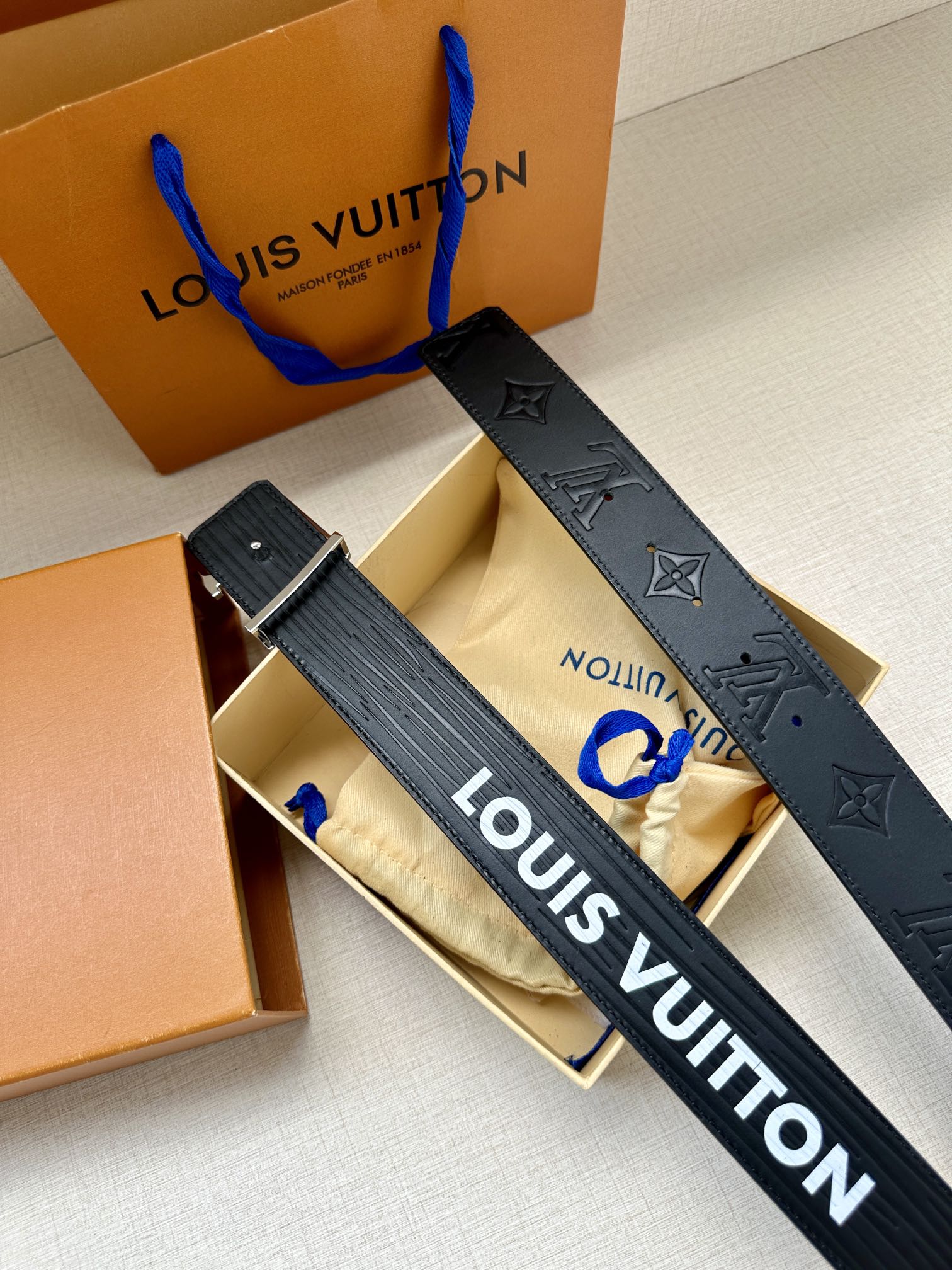 Louis Vuitton belt flat lay: dark blue embossed monogram strap with gold-tone LV buckle.