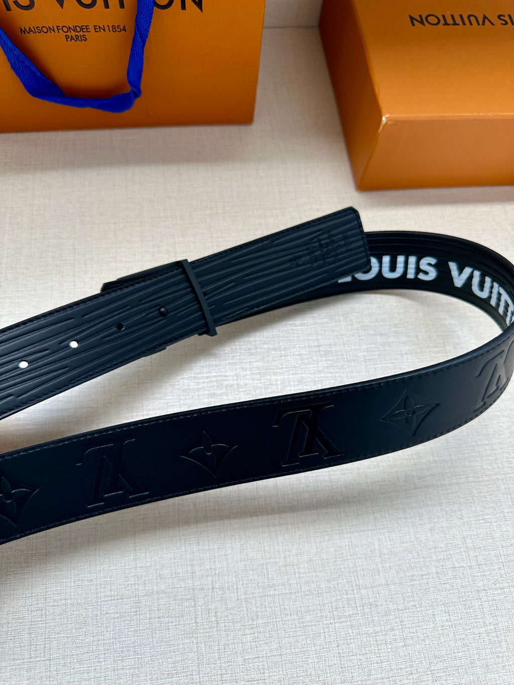 Dark gray leather belt with embossed monogram pattern, partial buckle view