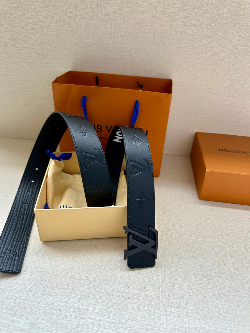 Dark gray embossed monogram belt with large silver-tone buckle, angled view