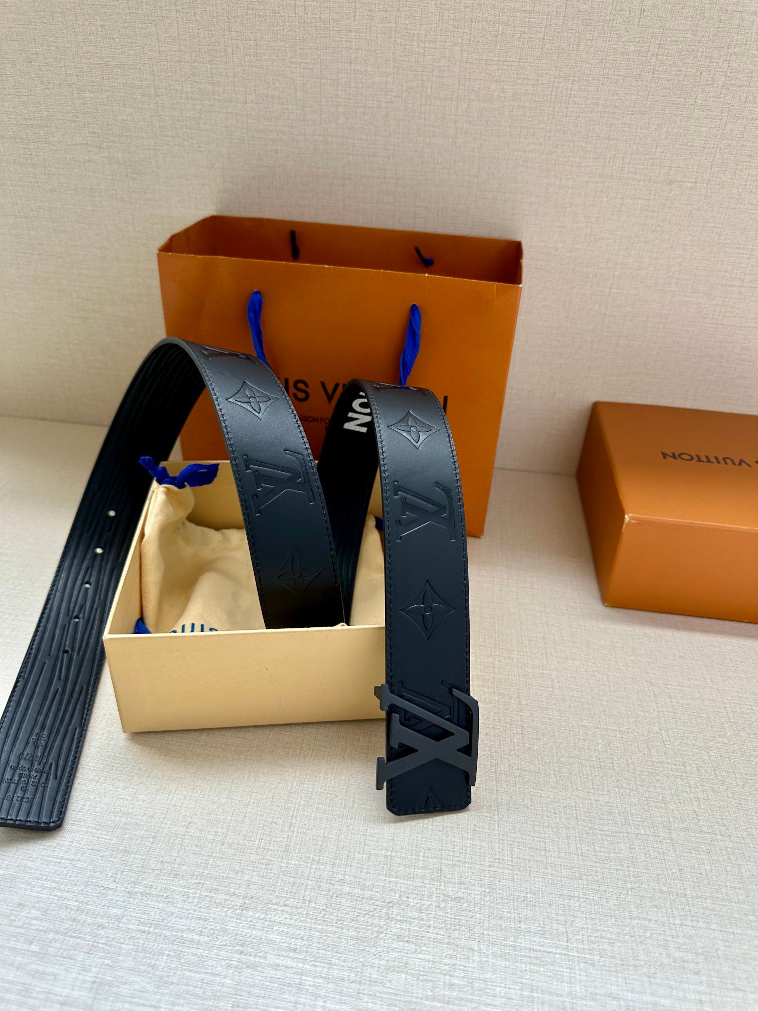 Dark gray embossed monogram belt with large silver-tone buckle, angled view