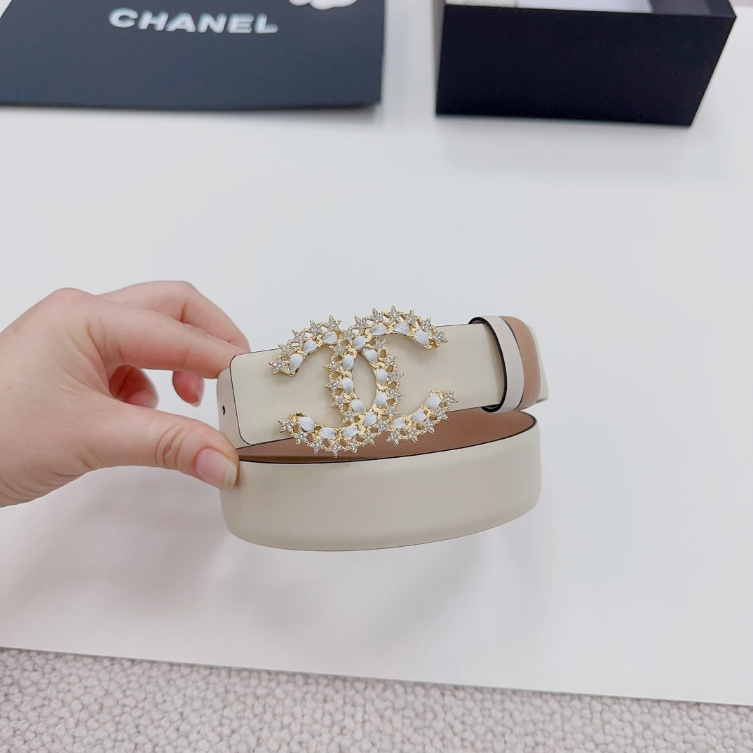 Beige leather belt held up, showing ornate gold-tone buckle with jeweled centerpiece.