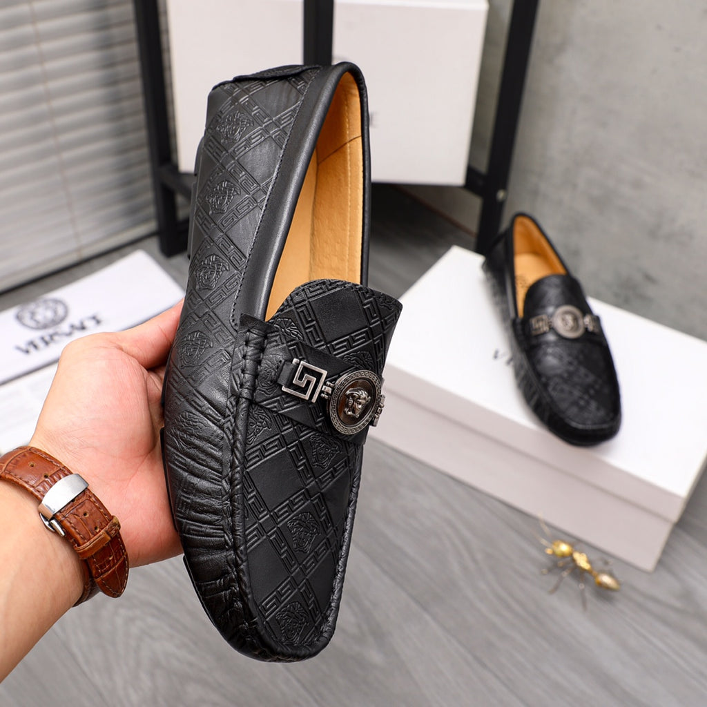 Black embossed leather loafer held in hand, gold buckle medallion on the vamp