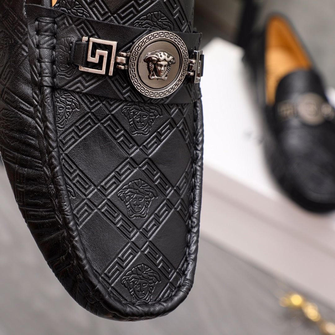 Close-up of black embossed leather loafer with gold buckle and medallion emblem