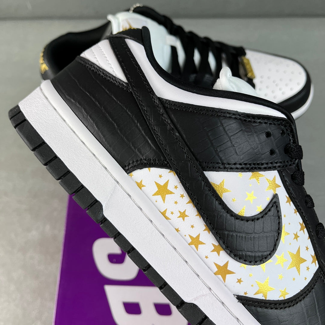 Black low-top sneaker with white toe panel, gold star Swoosh, and black outsole