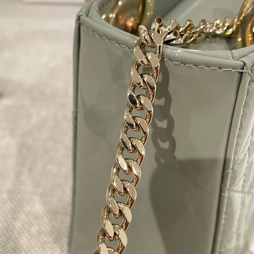 Sage green patent handbag with gold chain strap hardware and stitched panel