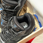 Black trainer sneaker close-up of laces and padded collar with tongue logo.