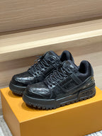 Black low-top lace-up trainer sneakers on a yellow box with rugged outsole.