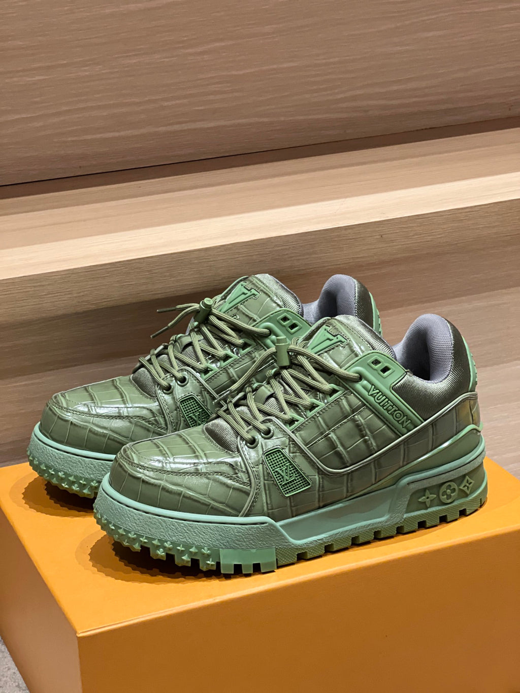 Green leather trainer sneakers on orange shoebox, lace-up with textured upper