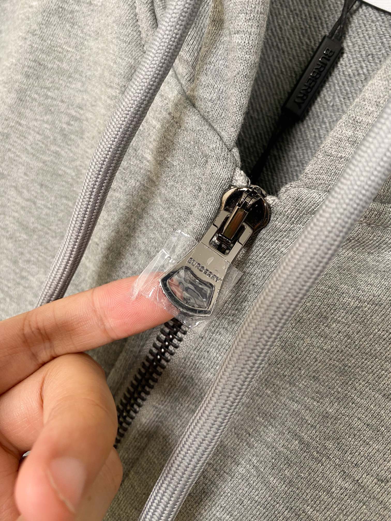 Zip-up hoodie zipper detail with metal pull and hood drawcord ends on heather gray