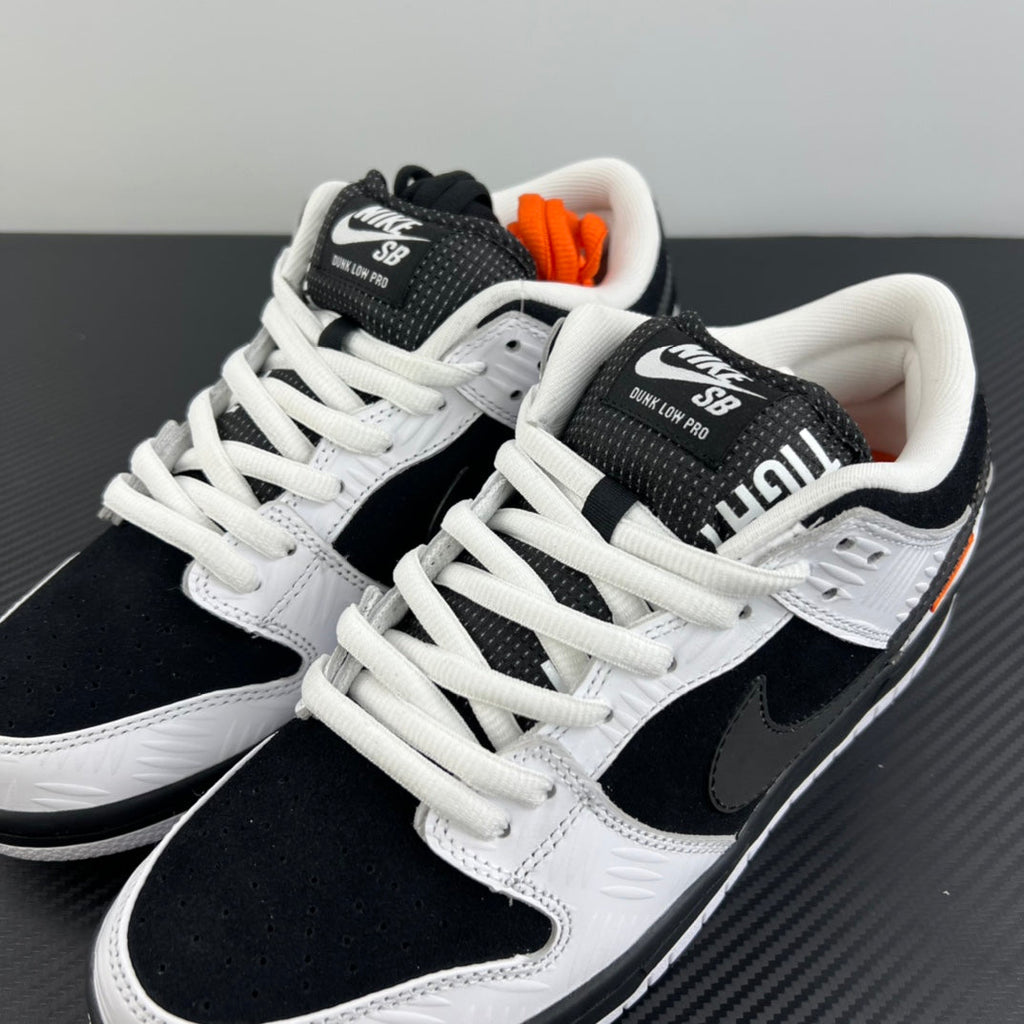 Two black and white low-top sneakers on their sides with white laces and orange heel detail