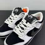 Two black and white low-top sneakers on their sides with white laces and orange heel detail