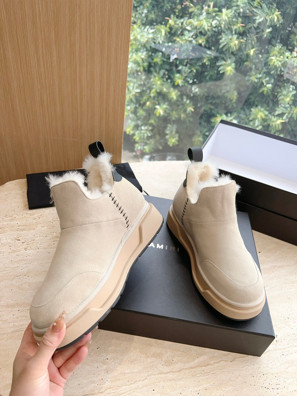 Amiri ankle boots in light beige suede with faux fur trim, shown with hand holding