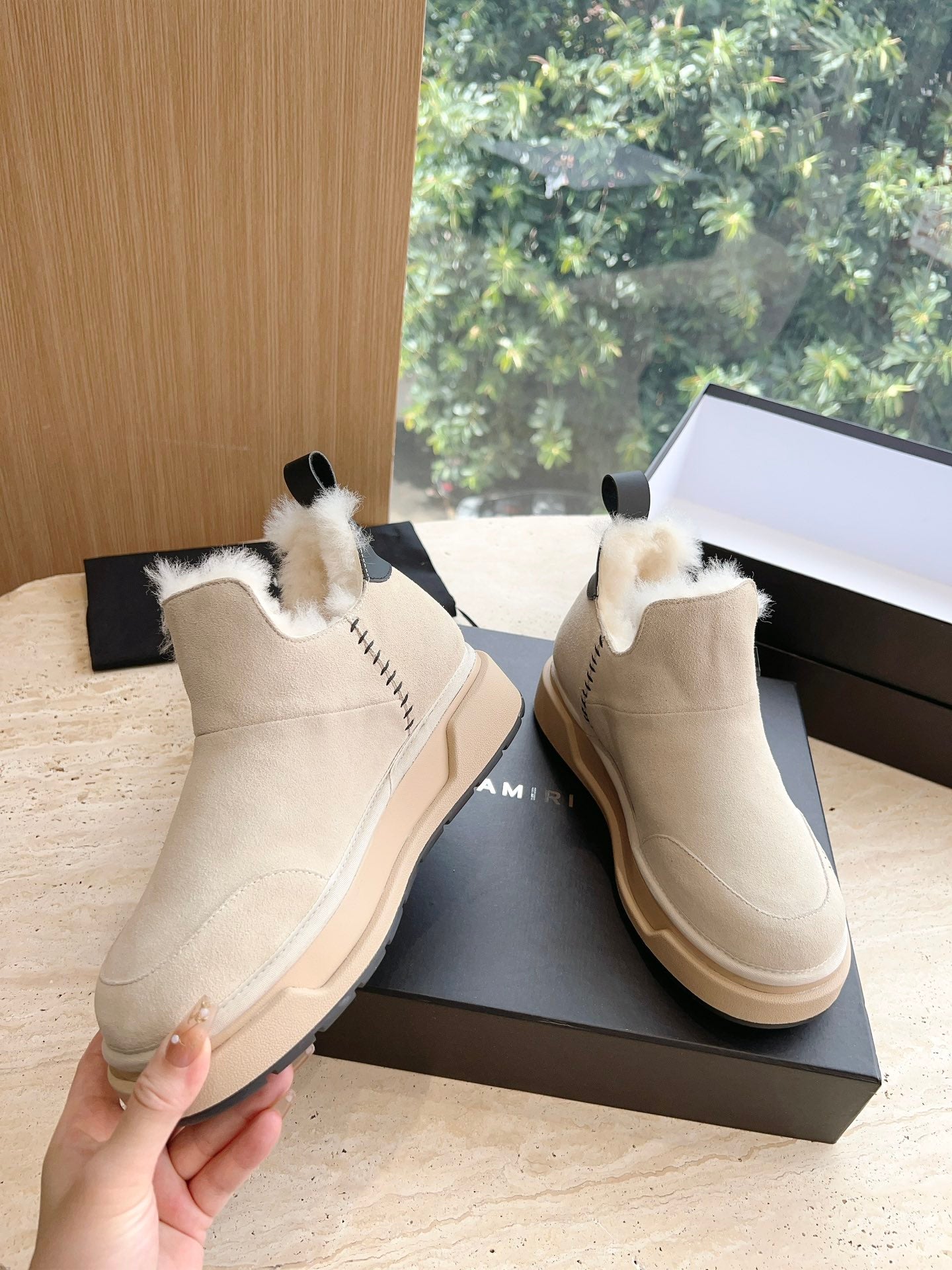 Amiri ankle boots in light beige suede with faux fur trim, shown with hand holding