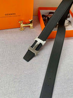 Black leather belt with gold H buckle and long strap, laid diagonally on fabric
