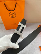 Hermes belt held up: black textured strap with metallic H buckle and keeper