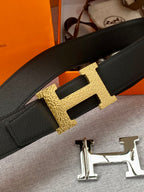 Hermes belt detail: black strap with gold H buckle and keeper tab