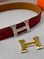 Hermes belt buckle close-up: gold H hardware on red textured strap.