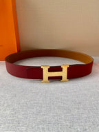 Hermes belt laid flat: red outer strap with gold H buckle and tan underside.