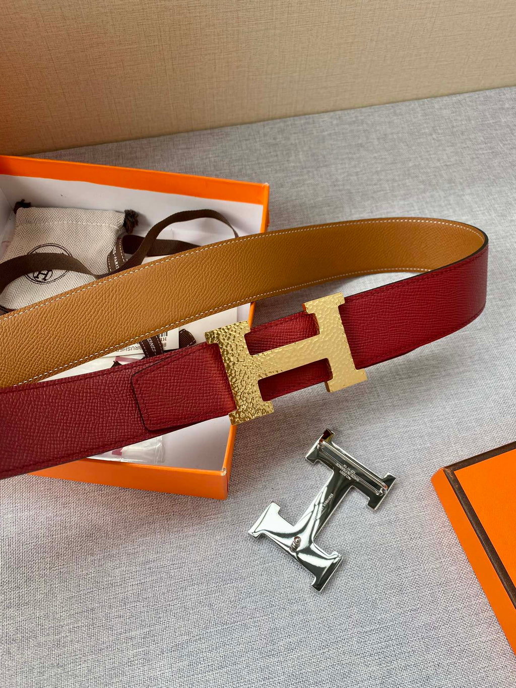 Red leather belt with gold-tone H buckle and tan strap on display