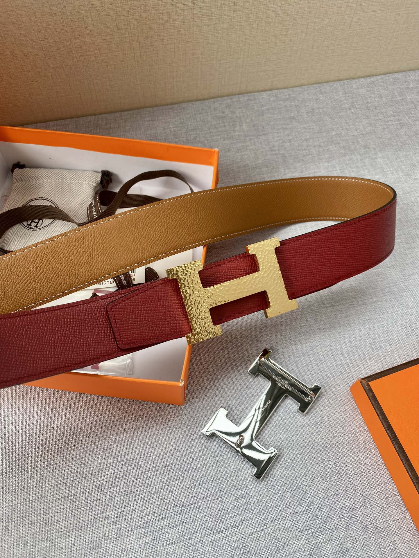 Red leather belt with gold-tone H buckle and tan strap on display