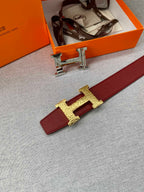 Hermes belt buckle detail: gold H hardware on red strap, metal keeper pieces.
