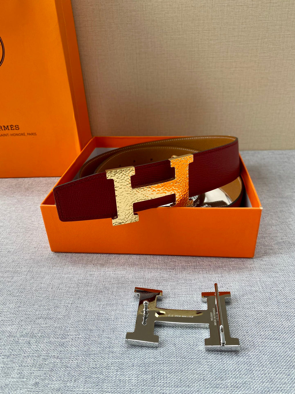 Red leather belt with gold-tone H buckle resting in a presentation box