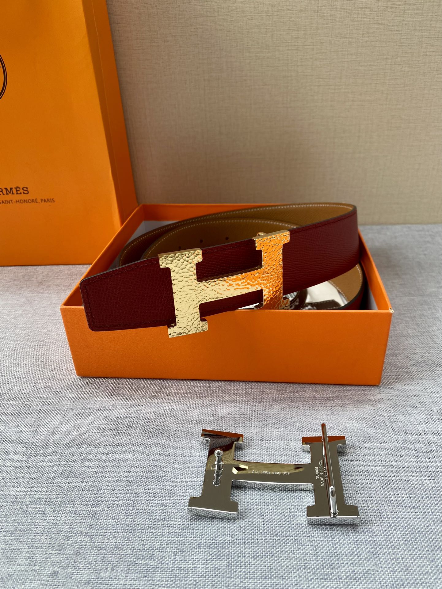 Red leather belt with gold-tone H buckle resting in a presentation box