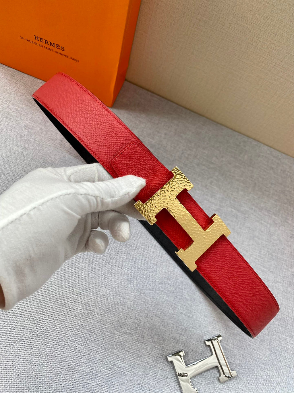 Red leather belt with gold-tone H buckle and red strap, held on a hand