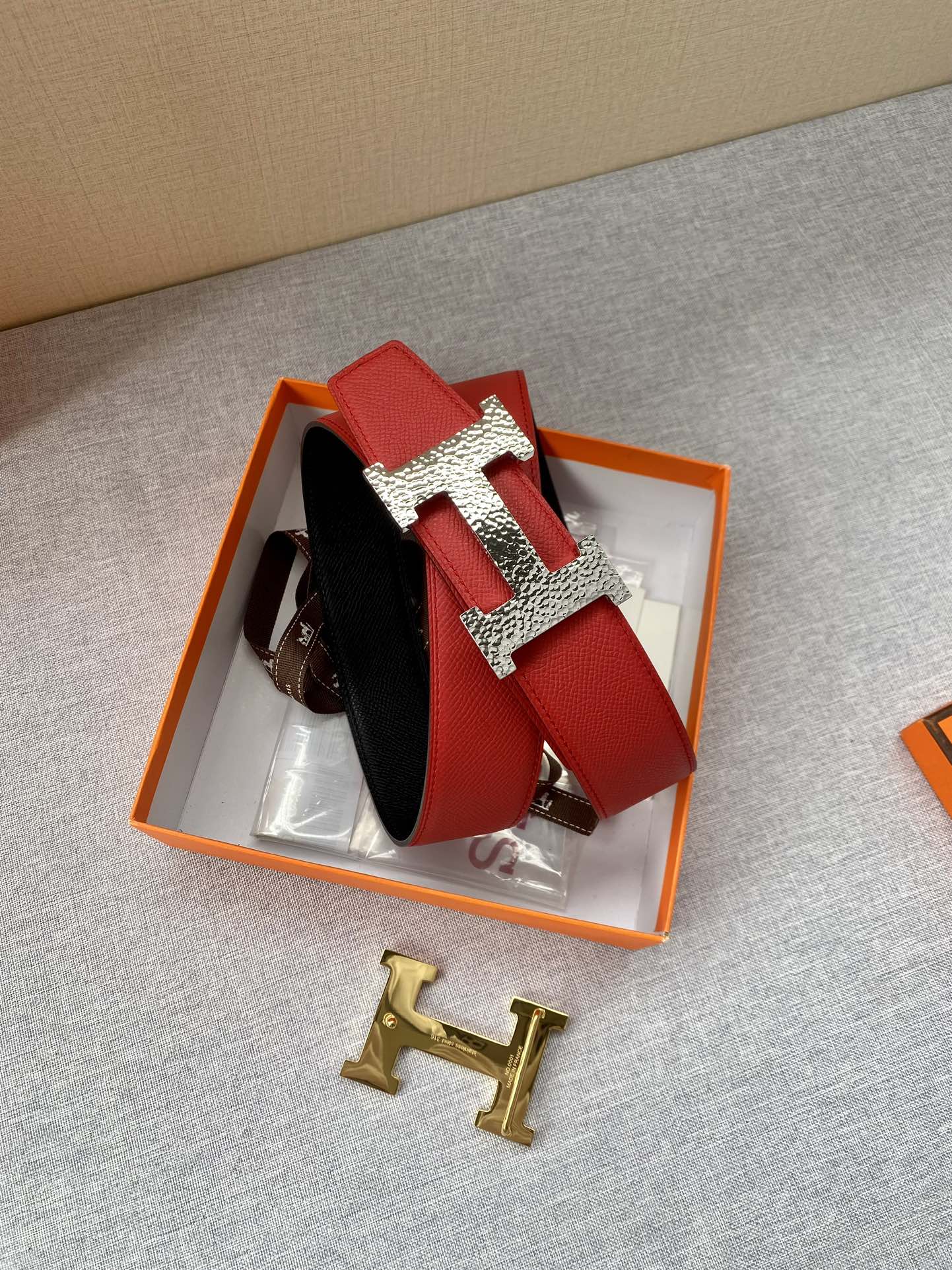 Red and black leather belt set in orange box with gold-tone H buckle hardware