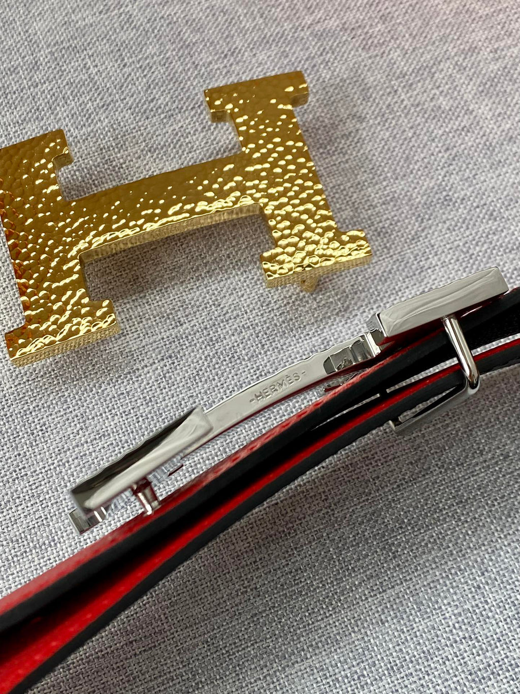 Gold-tone H belt buckle detail and metal tool pieces on fabric