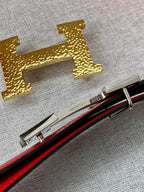 Gold-tone H buckle hardware on a red-and-black belt strap with silver frame