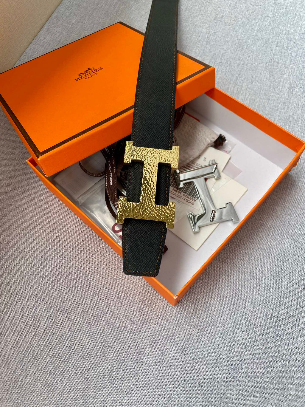 Leather belt with black strap and gold-tone H buckle, with extra hardware pieces