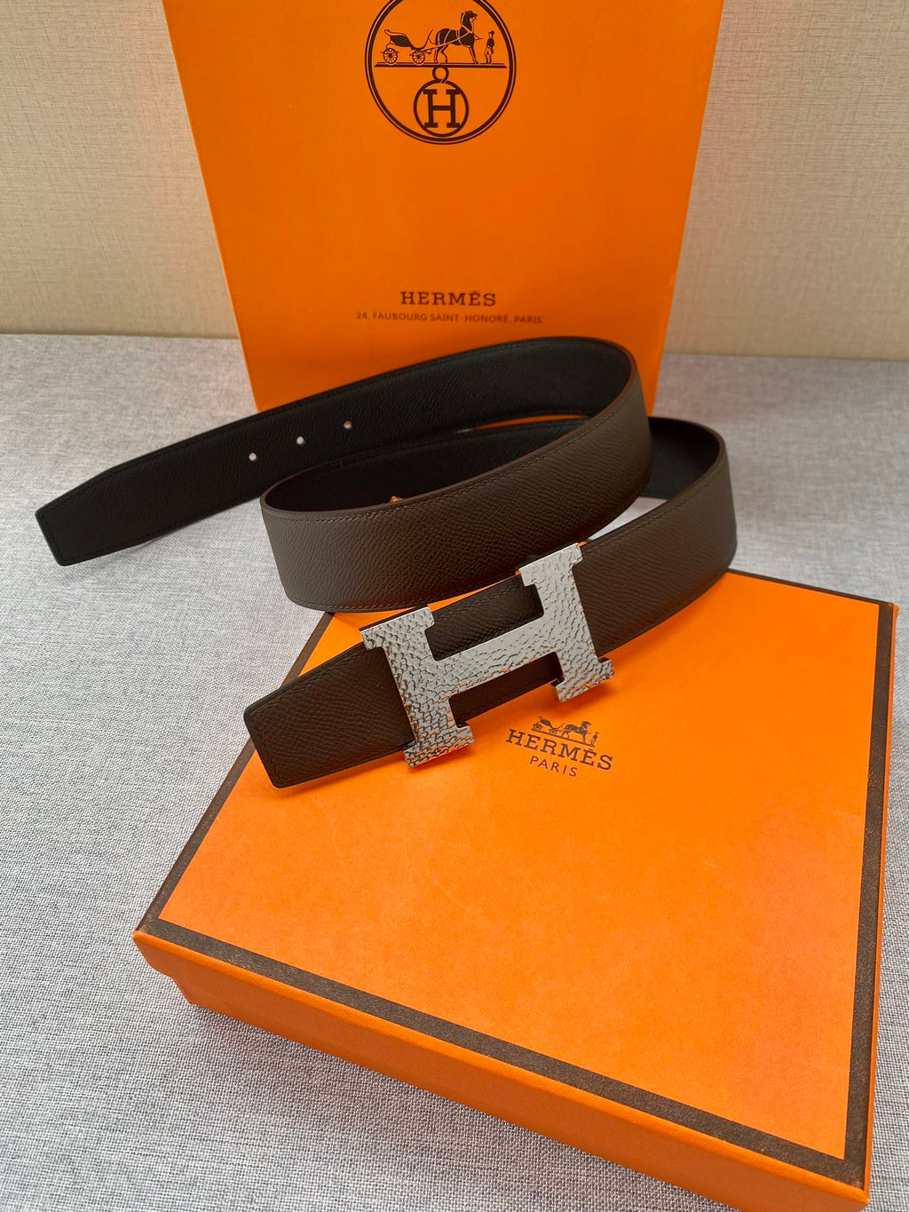 Hermes leather belt with dark strap and silver H buckle, flat view