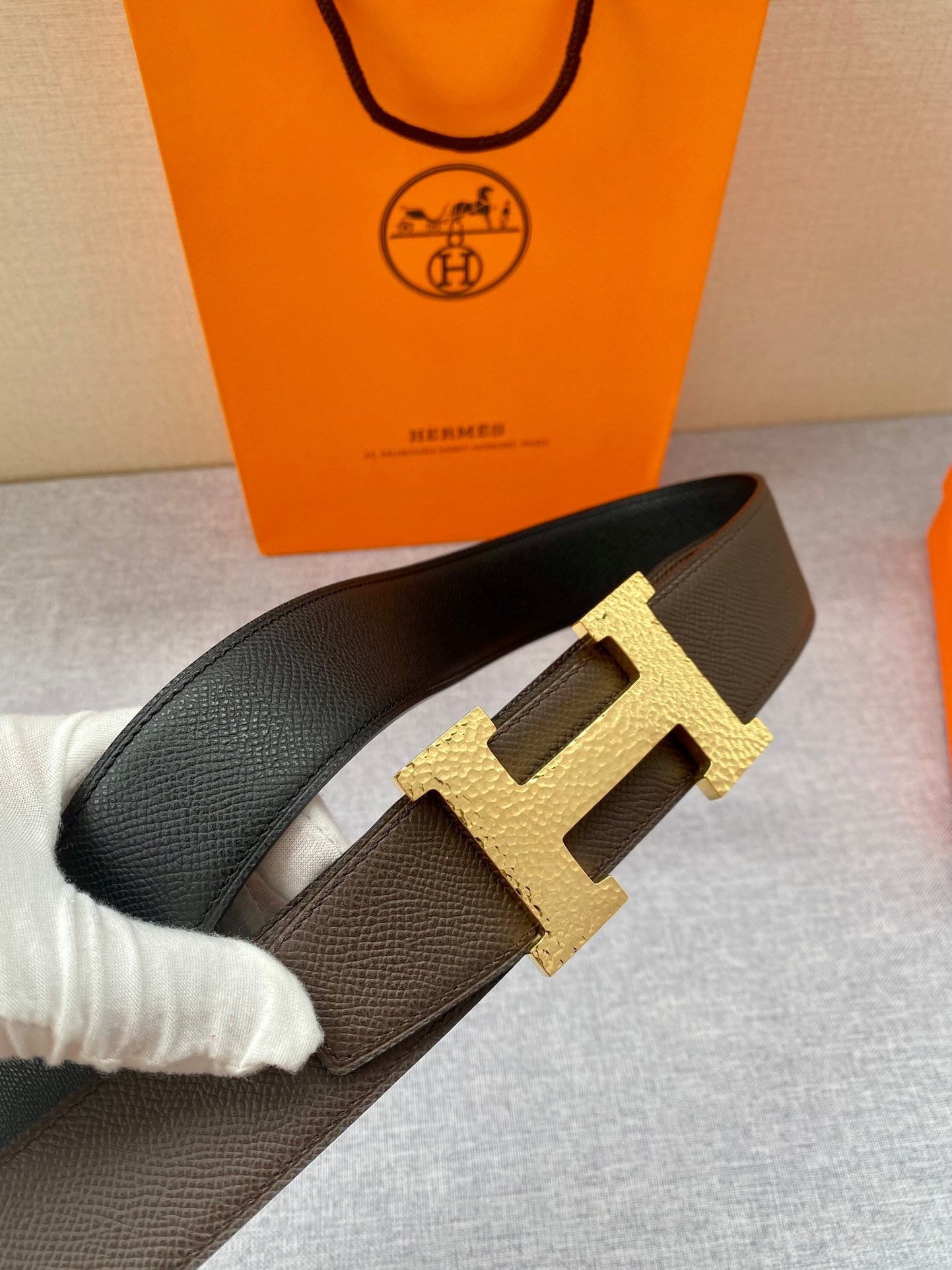 Hermes leather belt with dark strap and gold H buckle, close-up