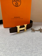 Brown leather belt with gold H buckle, with silver accessory pieces on table