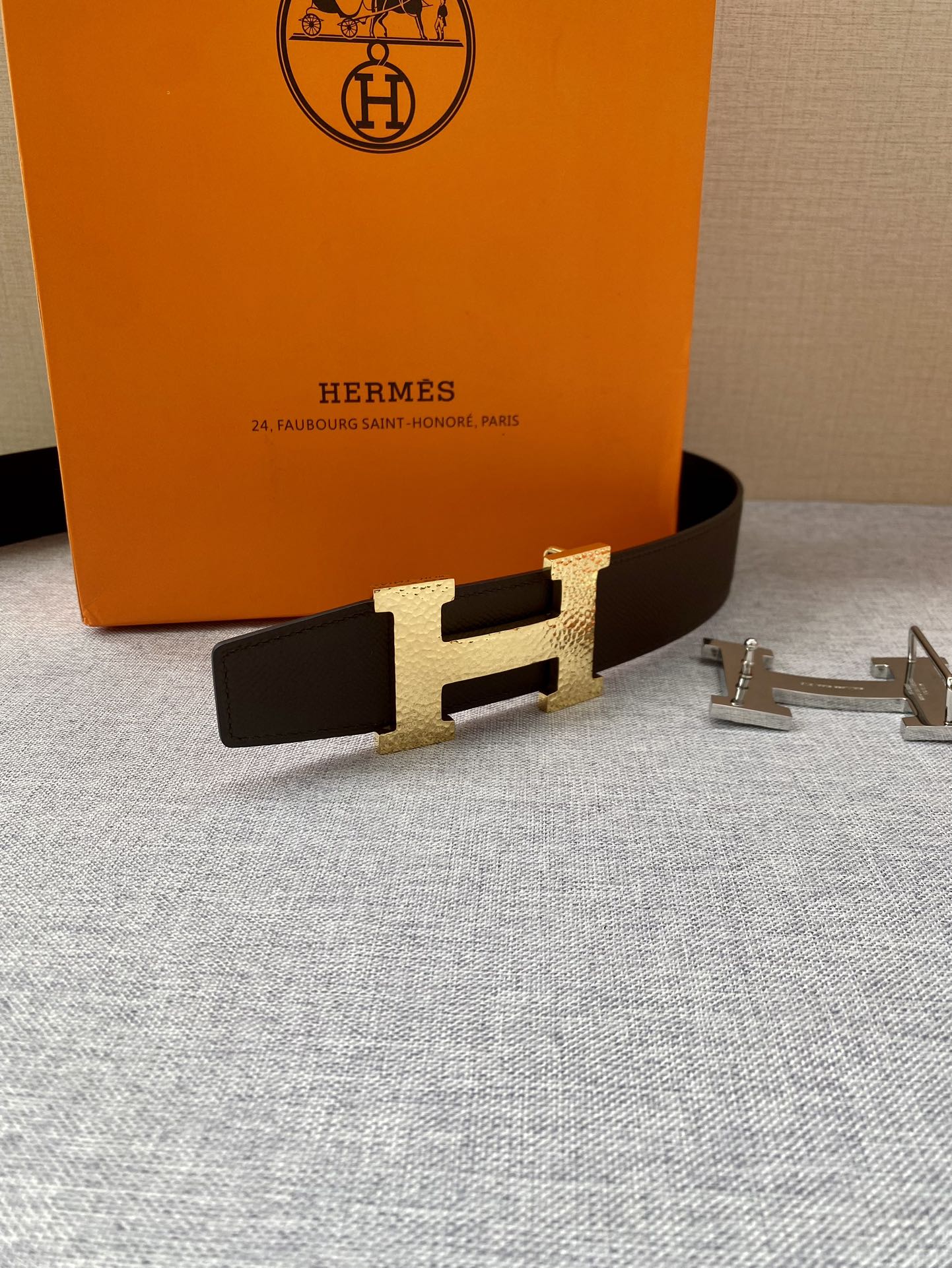Brown leather belt with gold H buckle, with silver accessory pieces on table
