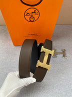 Brown leather belt with gold H and silver strap detail, side angle in hand