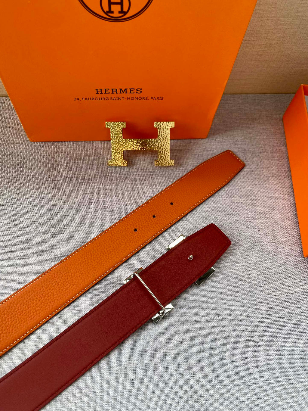 Orange leather belt strap with gold H logo buckle and punched holes