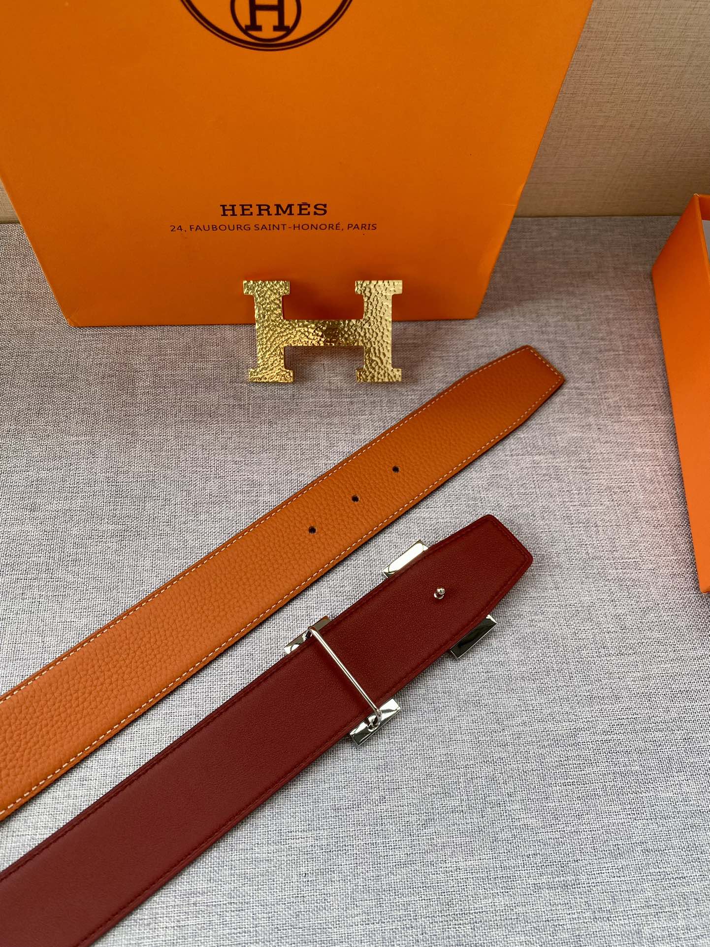 Orange leather belt strap with gold H logo buckle and punched holes