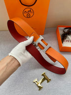 Orange leather belt with gold H buckle held in hand