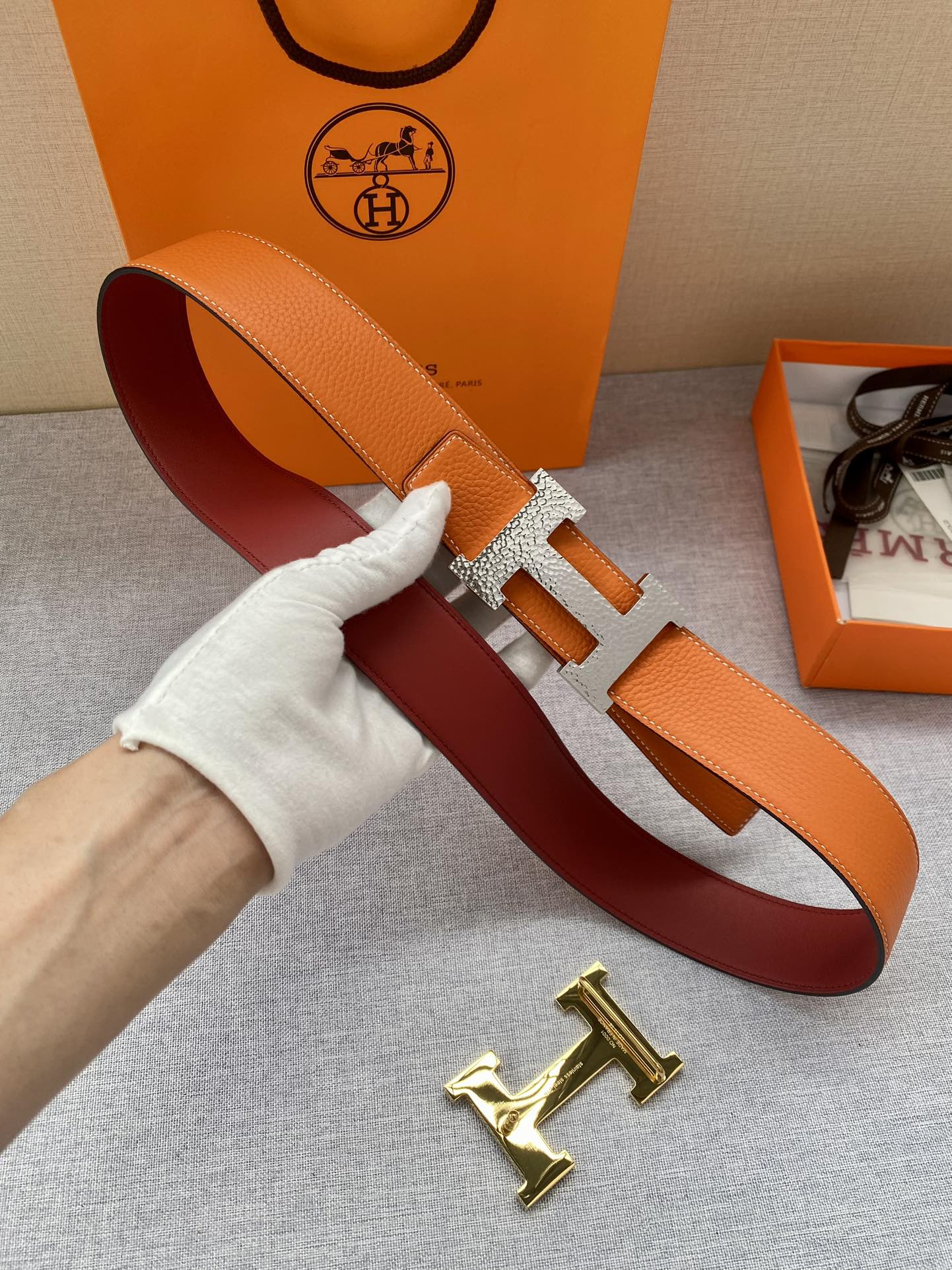 Orange leather belt with gold H buckle held in hand