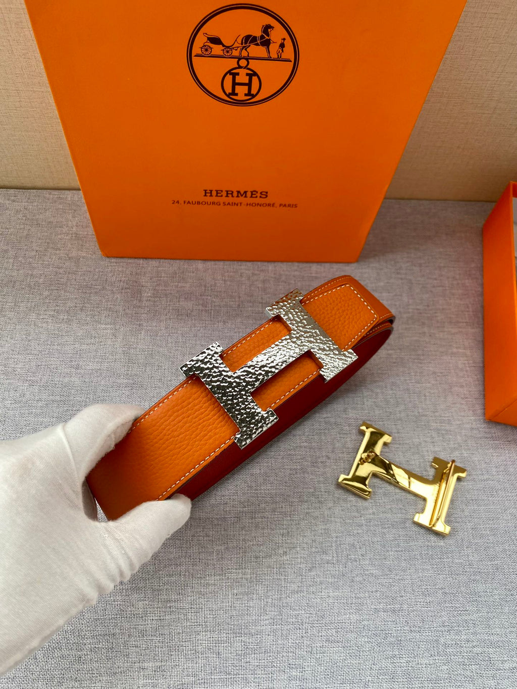 Orange leather belt with gold H buckle and rhinestone-style detailing
