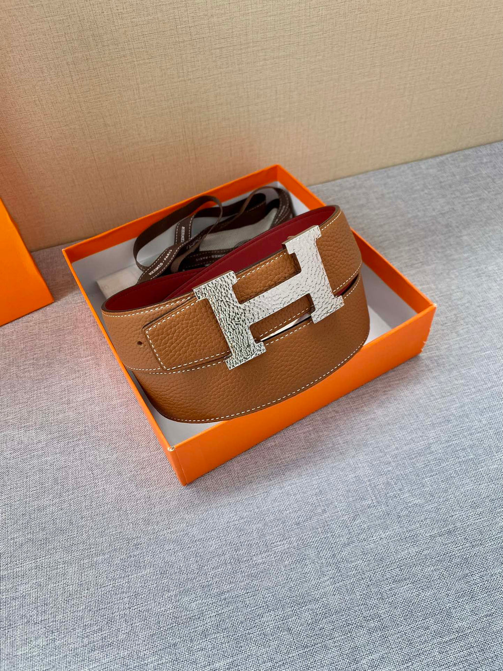 Brown leather belt with gold H buckle, laid flat
